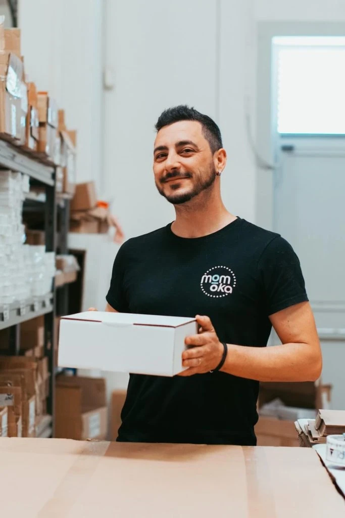 Operatore logistica Momoka sorridente mentre tiene un pacco per spedizione ecommerce, a testimonianza del customer care umano e professionale.