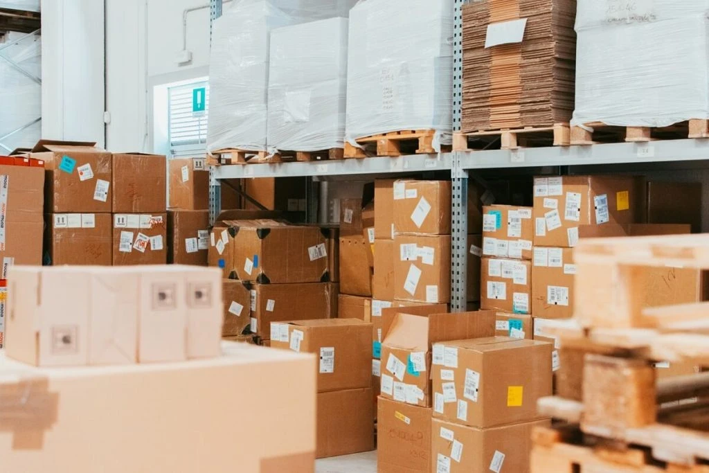 Vista ravvicinata di scaffalature industriali piene di scatole di cartone e bancali imballati in un magazzino logistico, a dimostrazione della corretta ottimizzazione degli spazi di stoccaggio e delle scorte.