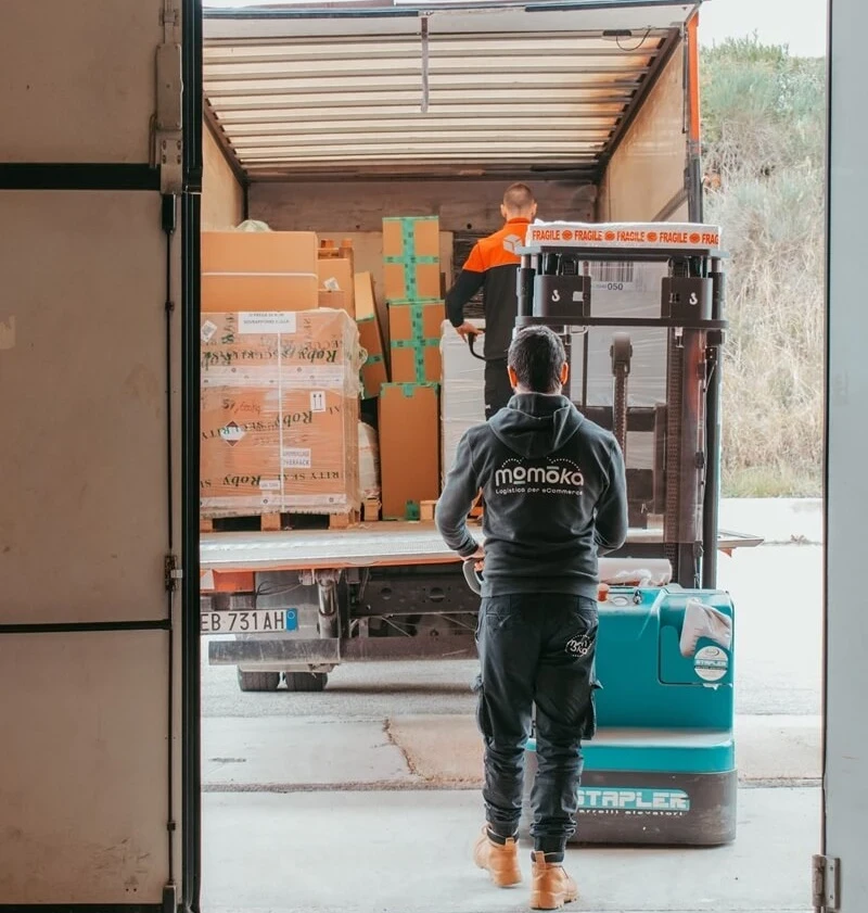 Operatore logistico Momoka con transpallet elettrico mentre carica un camion con pacchi pronti per la spedizione eCommerce, a conclusione del processo di pick and pack.