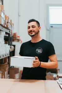 Operatore logistica Momoka sorridente mentre tiene un pacco per spedizione ecommerce, a testimonianza del customer care umano e professionale.