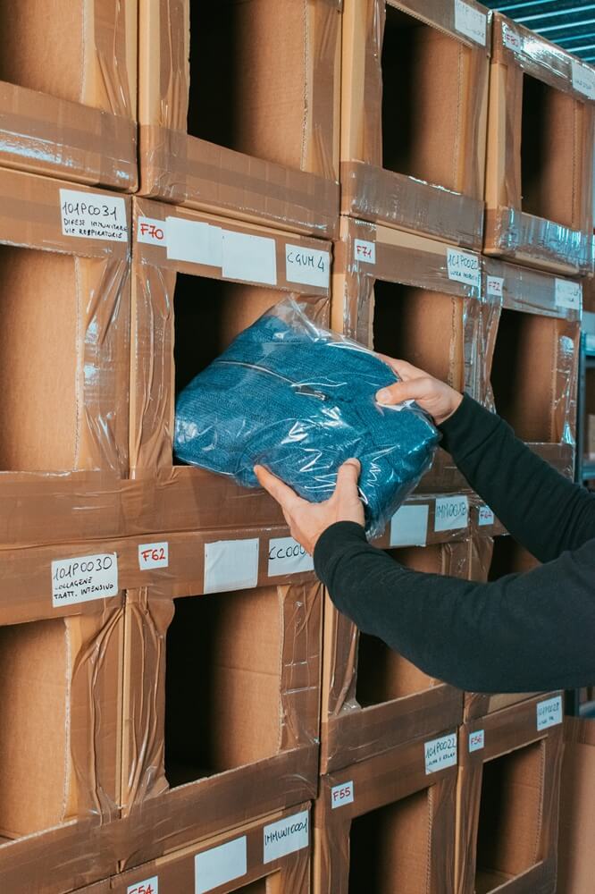 Operatore logistico di Momoka che preleva un capo d'abbigliamento confezionato da uno scaffale in magazzino per la spedizione.