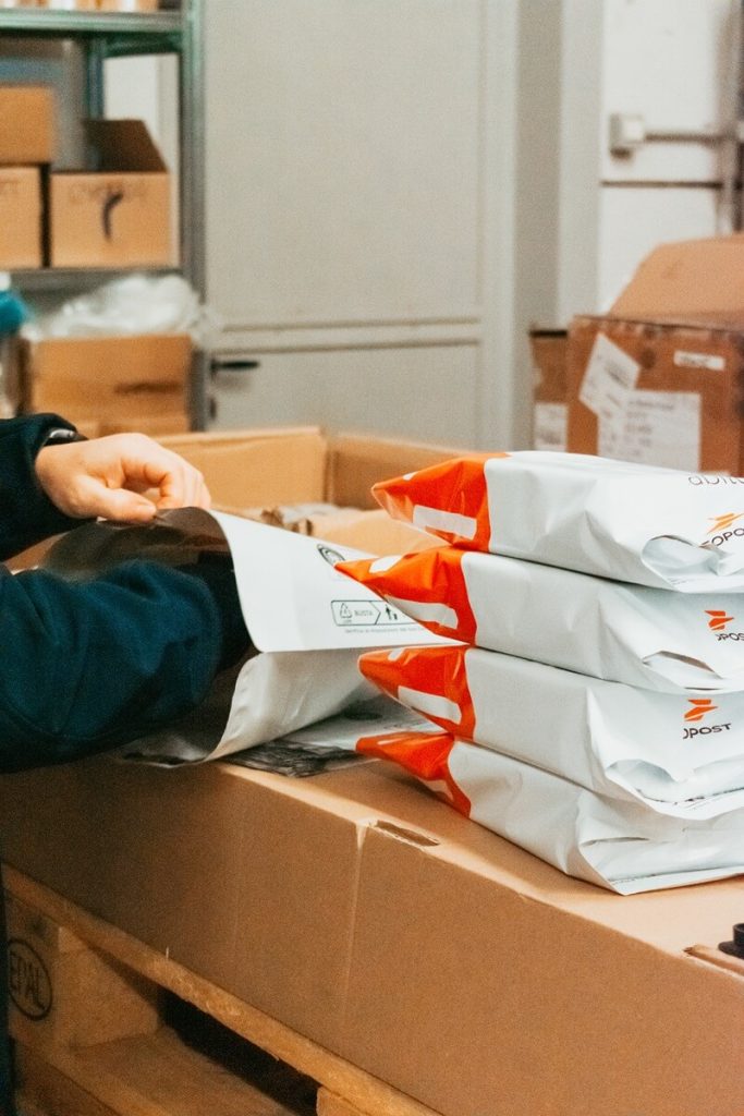 Dettaglio delle mani di un operatore mentre inserisce prodotti nelle buste di spedizione per l'ecommerce.