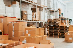 Ampia vista panoramica di un magazzino logistico Momoka ordinato, con alte scaffalature piene di scatole e bancali pronti per la spedizione e-commerce.