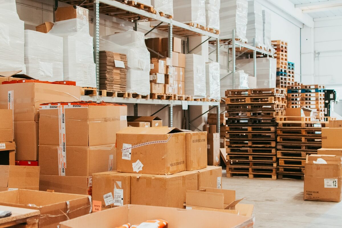 Ampia vista panoramica di un magazzino logistico Momoka ordinato, con alte scaffalature piene di scatole e bancali pronti per la spedizione e-commerce.